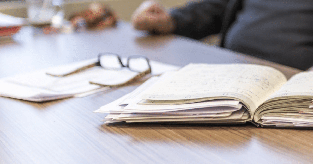 Imagen que muestra un cuaderno co apuntes, unos lentes de aumento y personas durante su descanso laboral