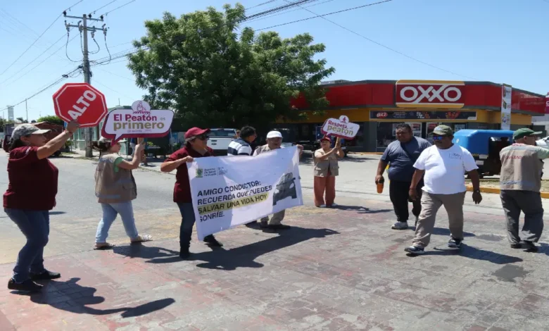 Personas participantes en una jornada de educación vial en Yucatán sostienen carteles con mensajes como “Alto” y “El peatón es primero”, en un cruce peatonal frente a un OXXO.